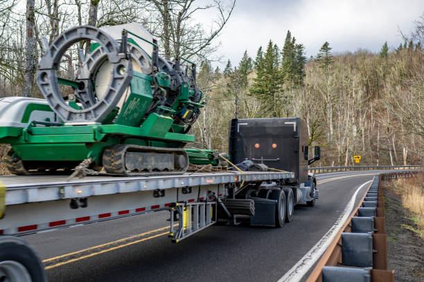 istock Black classic powerful big rig semi truck tractor transporting heavy cargo on flat bed semi trailer running on the winding mountain road with winter forest 2198488421