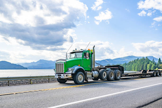 istock Heavy-duty green day cab big rig semi truck with empty step deck semi trailer running on the highway road along the Columbia River 2198488979