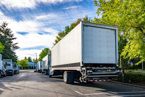 istock Middle duty day cab big rig semi trucks with box trailers and lifting platform in the back standing on the warehouse industrial parking lot on the one way city street 2198489357