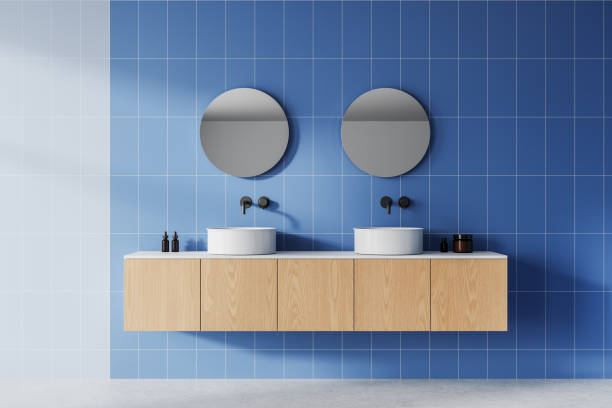 istock Modern bathroom with round mirrors and white sinks on wooden vanity against blue tiled wall. 3D Rendering 2198489640