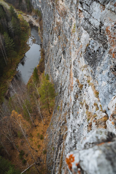This image captures an aerial perspective showcasing a dramatic rocky cliff that majestically rises over a beautiful river nestled in the background, creating a breathtaking natural scene