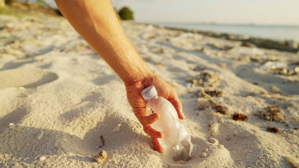 istock Hand collecting plastic bottle from the sand on polluted beach 2198498169