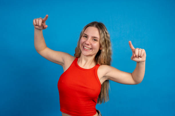 istock Young woman pointing with index fingers and smiling on blue background 2198501043