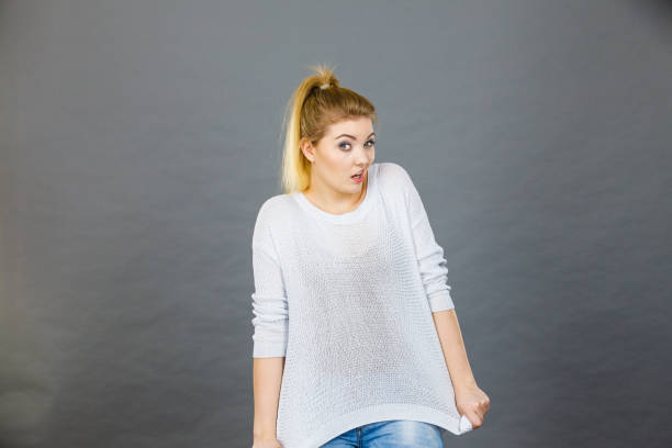 Woman wearing too big jumper, not fitting after weight loss. Grey background