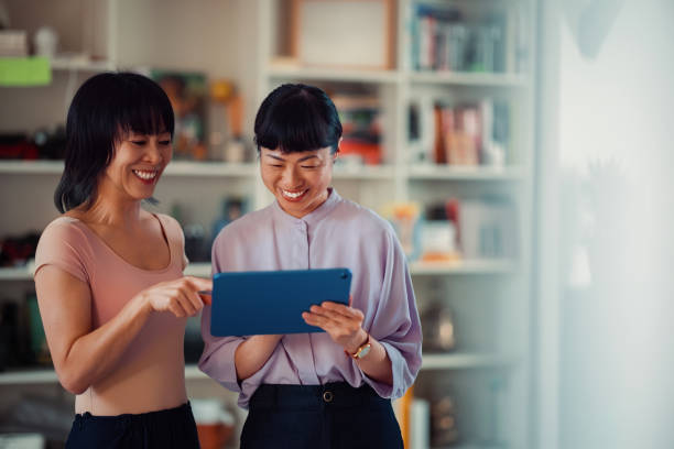 istock Two Women Smiling and Using a Tablet Device in a Bright Room 2198506520