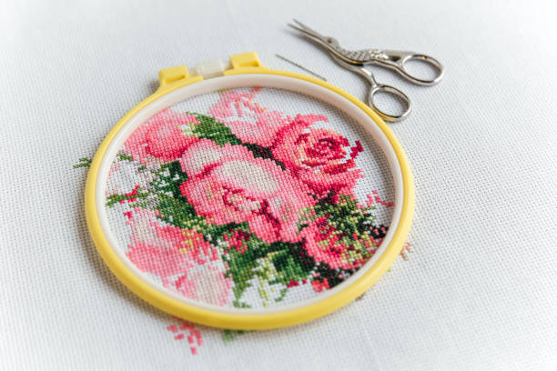 cross stitch process pink flowers in a yellow hoop on a white canvas aida 14 count, needle, vintage scissors for needlework