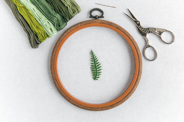 istock flat lay about cross stitch: a wooden hoop, a needle, scissors for needlework, green thread floss and a small green sprig of fern on a white canvas aida 16 count 1 2198512095