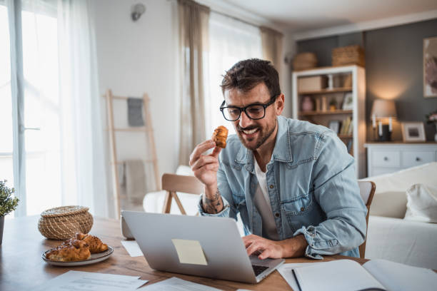 istock Young man enjoying a croissant while working in his home office 2198514459