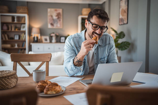 istock Young man enjoying a croissant while working in his home office 2198514463