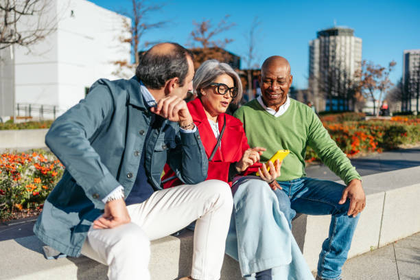 istock Group of smiling mature friends sitting outdoors using a smartphone 2198514596