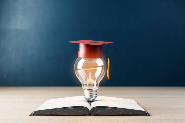 istock Graduation cap on light bulb over open book on wooden table, blue background, symbolizing education and knowledge. 3D Rendering 2198518911