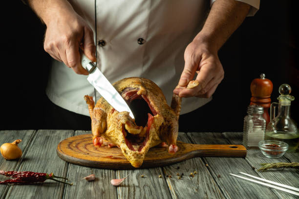 istock A skilled chef carves a raw duck carcass that rests on a rustic wooden board. Fresh ingredients and spices surround the scene, hinting at the passion for culinary art in a cozy kitchen 2198522094