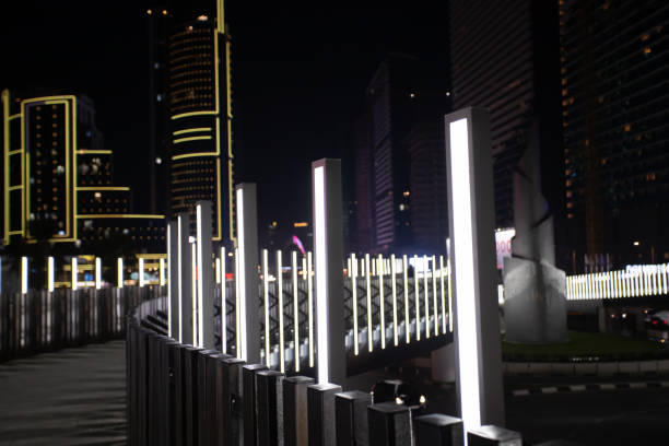 istock Night view of a modern cityscape featuring glowing light poles along a curved pathway, with tall buildings in the background. 2198522301