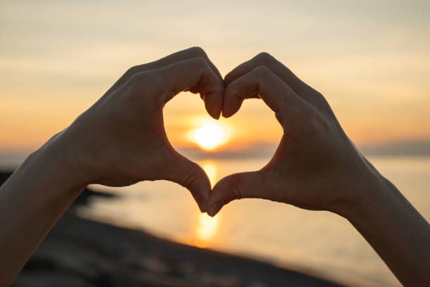 istock Hands making Heart Shape at Sunset, romantic reflection of sunlight on calm water, scenic horizon blending with the serene sky 2198522317