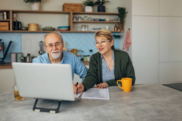 istock Smiling senior couple sitting at the kitchen table looking at their online finances and using technology to make financial plans for their retirement income 2198522971
