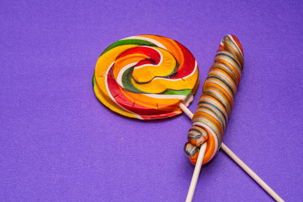 Colorful spiral lollipops on purple background. The flat lay composition for confectionery, childhood, or festive designs.