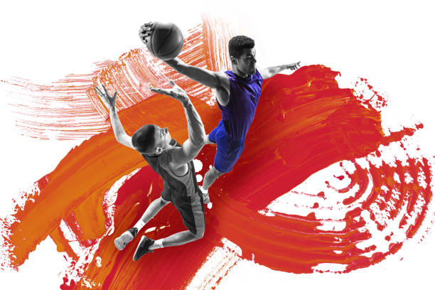 istock Modern art design. Basketball player in blue uniform soaring with ball, defender attempting block against fiery orange and red brushstroke background. 2198523867