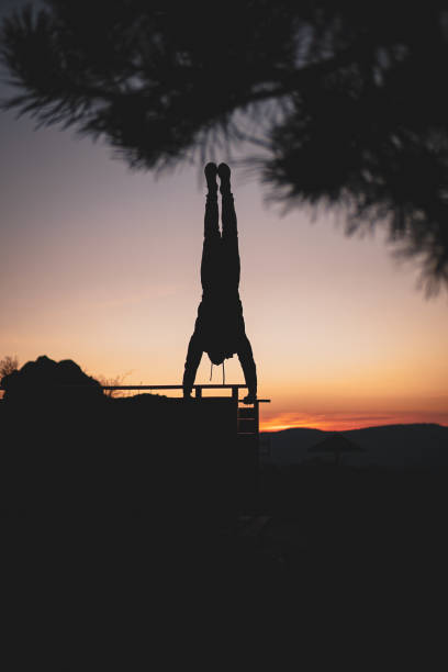 Person doing extreme hand standing, upside down. Silhouette. Doing handstand on egde of a viewpoint on a mountain, street workout, calisthenics
