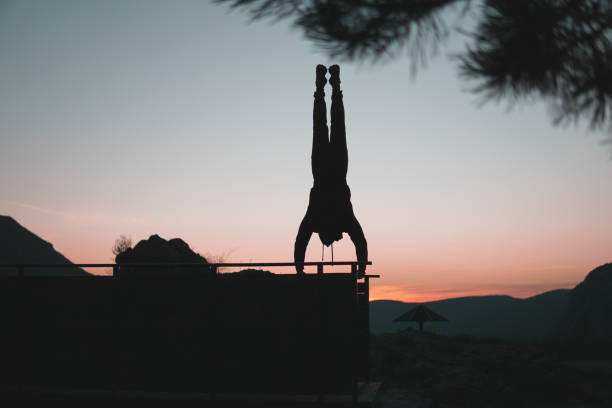 Person doing extreme hand standing, upside down. Silhouette. Doing handstand on egde of a viewpoint on a mountain, street workout, calisthenics