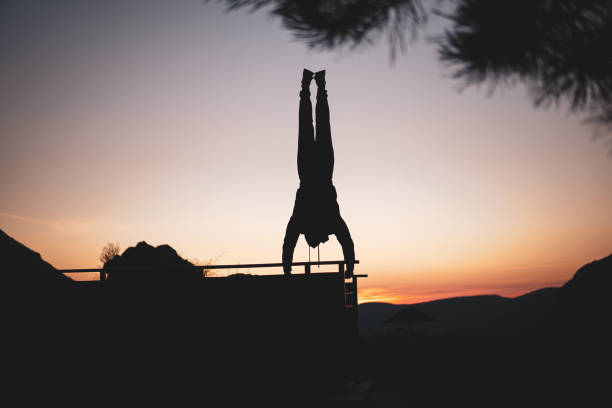 Person doing extreme hand standing, upside down. Silhouette. Doing handstand on egde of a viewpoint on a mountain, street workout, calisthenics
