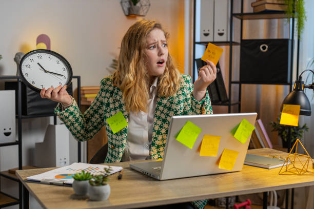 istock Tired businesswoman using laptop sticky notes with many tasks overworked checking time on clock 2198527650