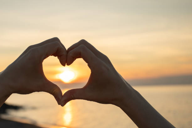 istock Hands making Heart Shape at Sunset, tranquil golden hour on the sea, peaceful gesture symbolizing love and emotion outdoors 2198531978