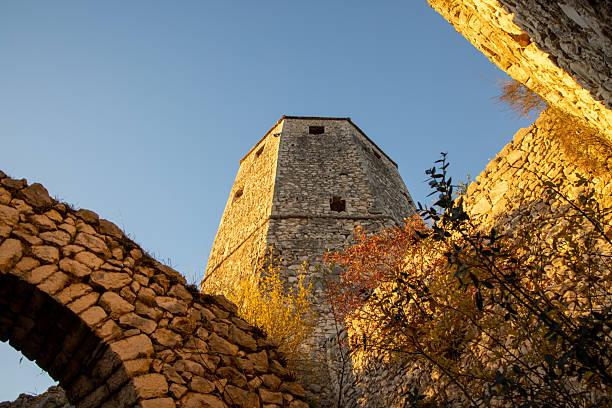 An old stone tower stands majestically under clear blue skies, surrounded by vibrant autumn leaves, showcasing the harmony between architecture and nature.