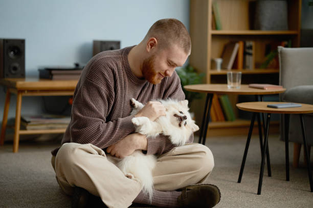 istock Man Cuddling Fluffy Dog in Cozy Living Room Setting 2198546096