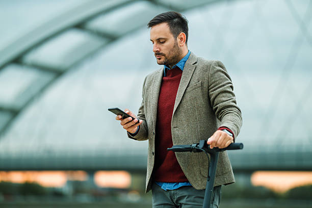 istock Man in Blazer with Smartphone Standing by Electric Scooter 2198546197