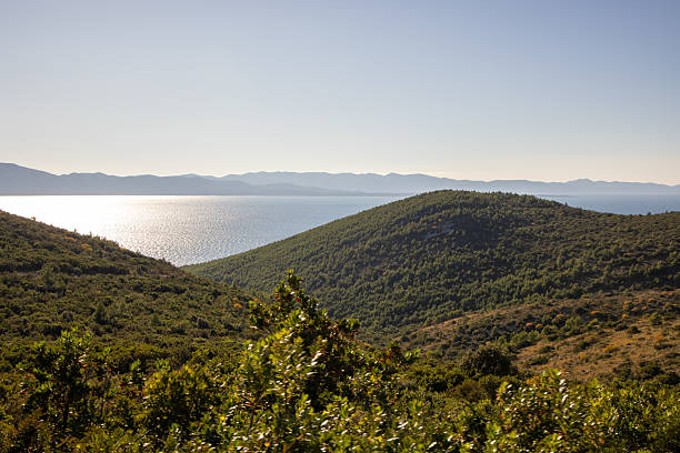 This captivating coastal landscape features dynamic hills meeting a sparkling sea under brilliant sunlight, embodying the essence of serene outdoor adventures and nature's beauty.