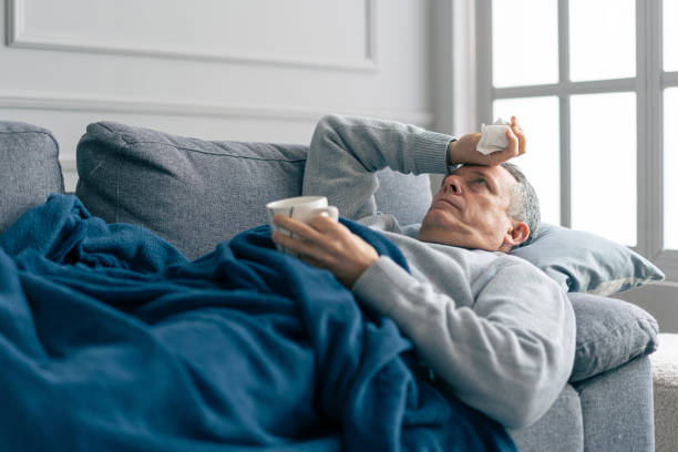 istock Man Resting on Couch with Blanket, Feeling Unwell While Holding a Mug in Hand 2198548904