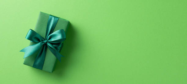istock Green wrapped gift box with a satin dark green decorative ribbon, presented on a matching flat green surface 2198550720