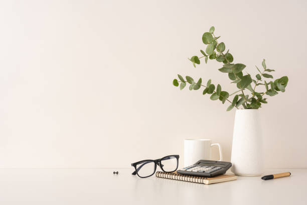 istock Minimalist workspace featuring glasses, a calculator, notebook, pen, and a eucalyptus plant on a table 2198550793