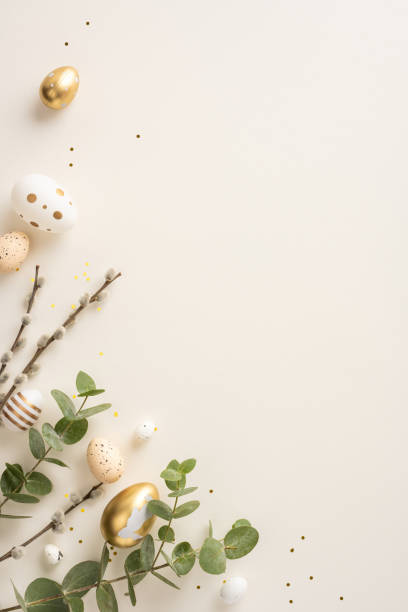 Easter vertical eggs in gold, white, and pastel colors placed with green branches on a beige background, evoking a sense of spring and festivity