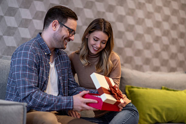 istock Smiling Couple Enjoying Opening a Gift Together on a Couch 2198553366
