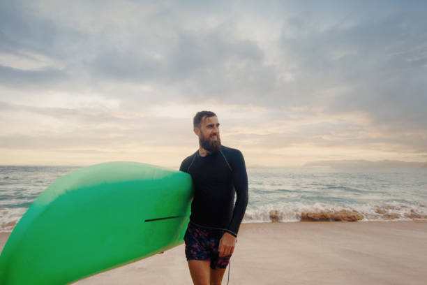 istock Young  bearded man with surfboard standing near a beach. Man with surfing board outdoors on a summer day. 2198555302