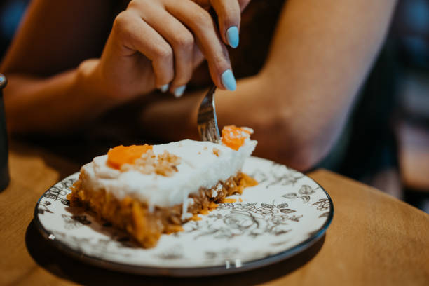 Woman enjoying a slice of carrot cake in a cafe Woman eating delicious piece of carrot cake in cozy cafe carrot cake day stock pictures, royalty-free photos & images