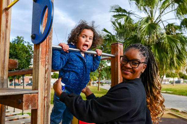 istock Mother helping daughter playing on monkey bars in playground 2198557038