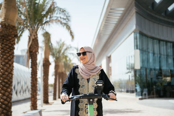 istock Smiling Arabic woman using electric scooter in the downtown 2198557522