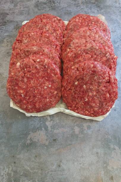 istock Above, raw beef patties rest on paper placed on a concrete table. Negative space, portrait. 2198559710