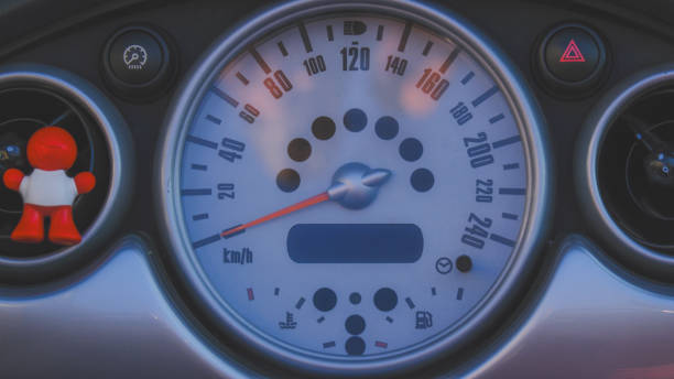 A car dashboard with a speedometer showing a speed of 120 km/h. A small orange figure is sitting on the speedometer