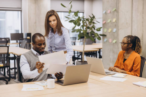 istock Colleagues collaborating, reviewing paperwork on laptops during team meeting in modern, sunlit workspace 2198564037