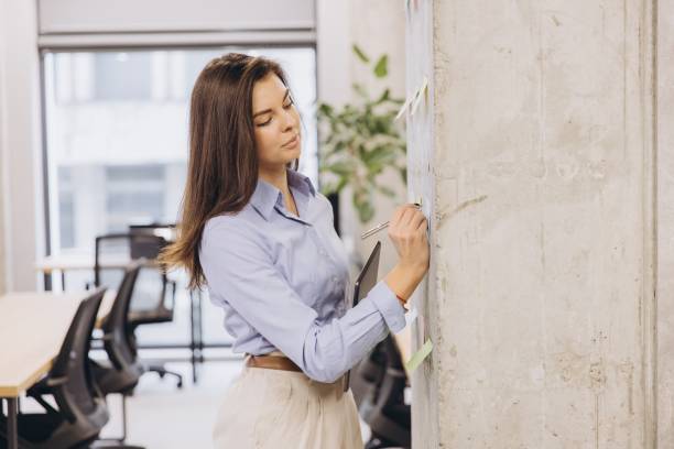 istock Businesswoman taking notes on sticky notes attached to a concrete wall in a modern office 2198564137