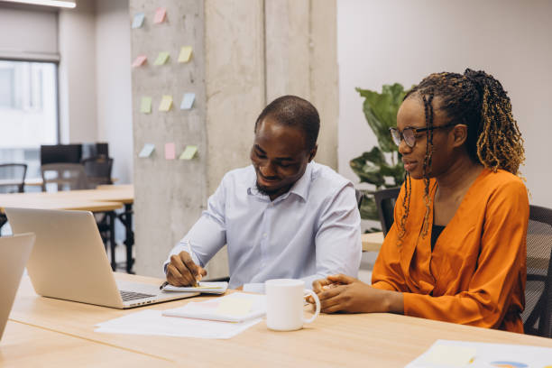 istock Two african american business people working together in modern office, using laptop and taking notes 2198564310