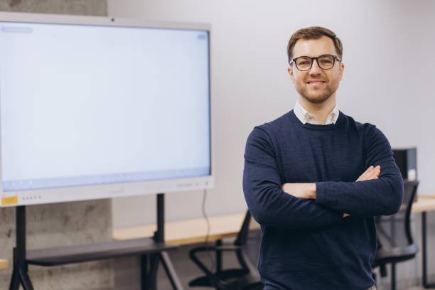 istock Professional businessman smiling, crossing arms while standing in sleek workspace near blank interactive display screen 2198564613