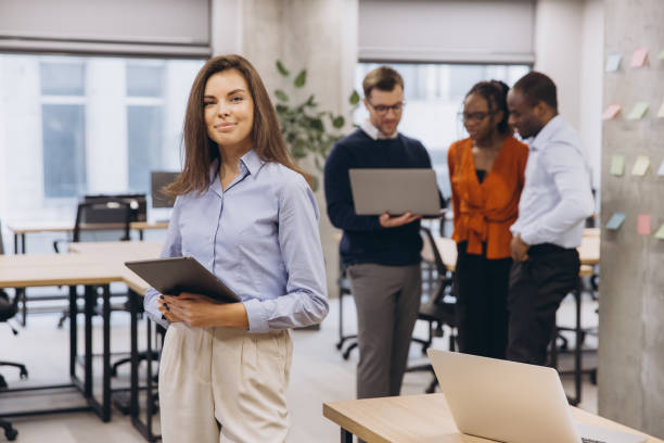 istock Businesswoman holding tablet smiling with multi ethnic colleagues working together using laptops in background in modern office 2198565348