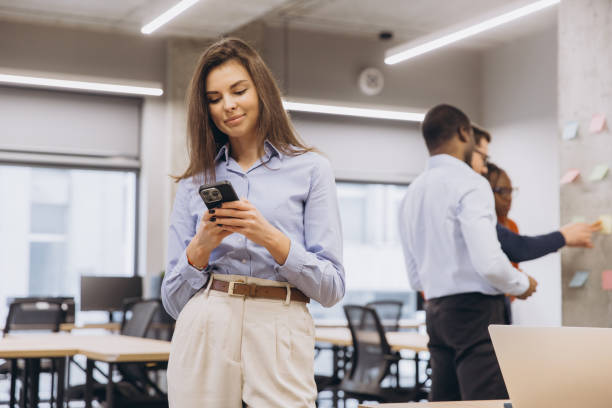 istock Businesswoman using mobile phone in modern office while colleagues working together on project in background 2198565357