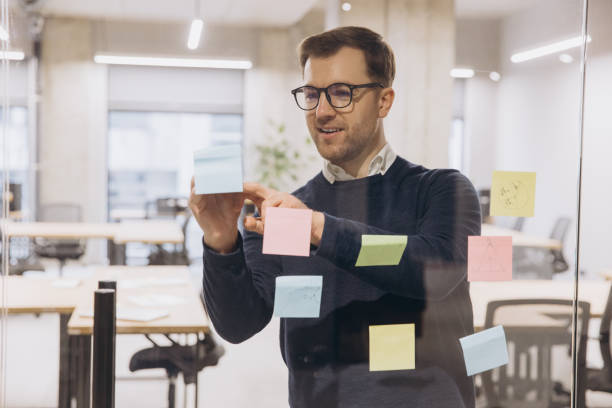istock Professional man workplace team member organizing multicolored sticky notes on glass partition, collaborating during strategic planning session 2198568316