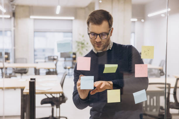 istock Professional man using colorful sticky notes on glass wall in modern office, planning and organizing tasks for a project 2198568322