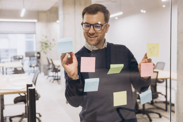 istock Business professional brainstorming ideas using colorful sticky notes on glass wall in modern office environment with open workspace 2198568333